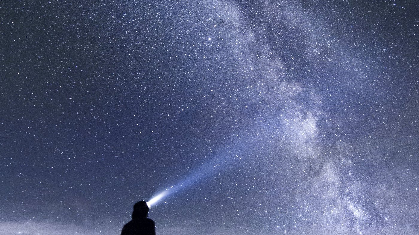 Hiker using a headlamp under a clear night sky in mountain terrain