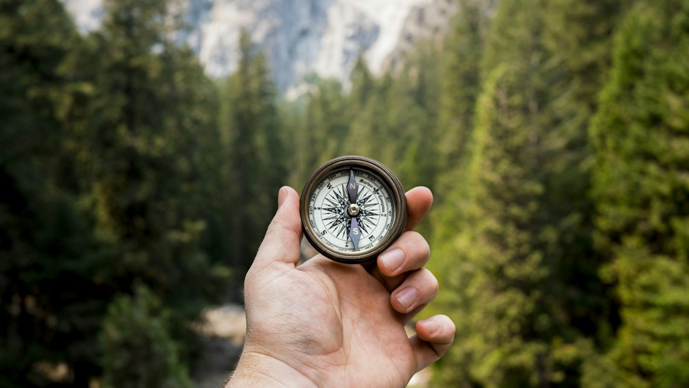 Hand holding a compass on a forested mountain trail