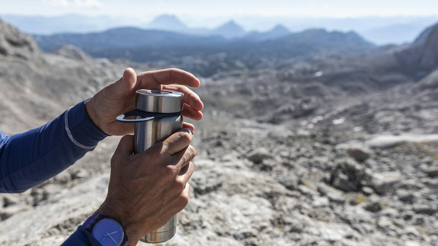Reusable water bottle held on a mountain route above rocky terrain